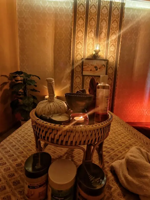 Herbal compress ball, oils and scrub jars on a rattan table in a warm-lit massage room