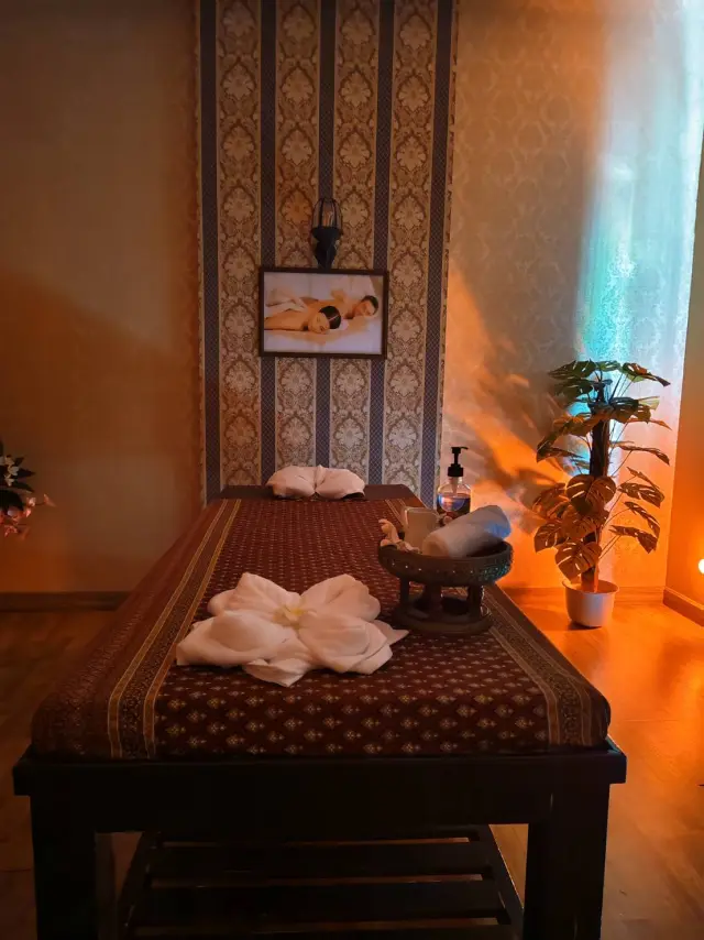 Treatment room with a massage bed, plant and folded towel flower at Ai Oon Massage Lanna