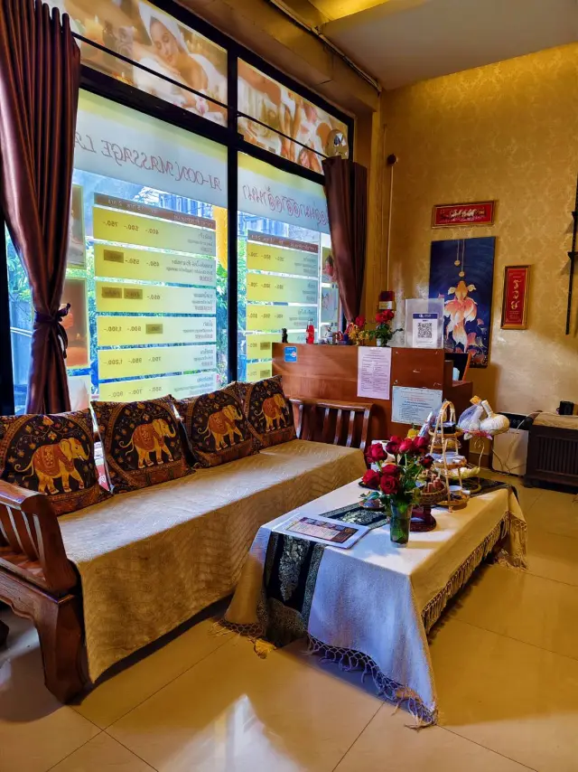 Reception seating area with an elephant-print sofa and price boards at Ai Oon Massage Lanna