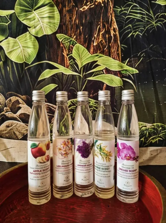 Five bottles of scented aromatherapy massage oil in front of a tropical leaf backdrop
