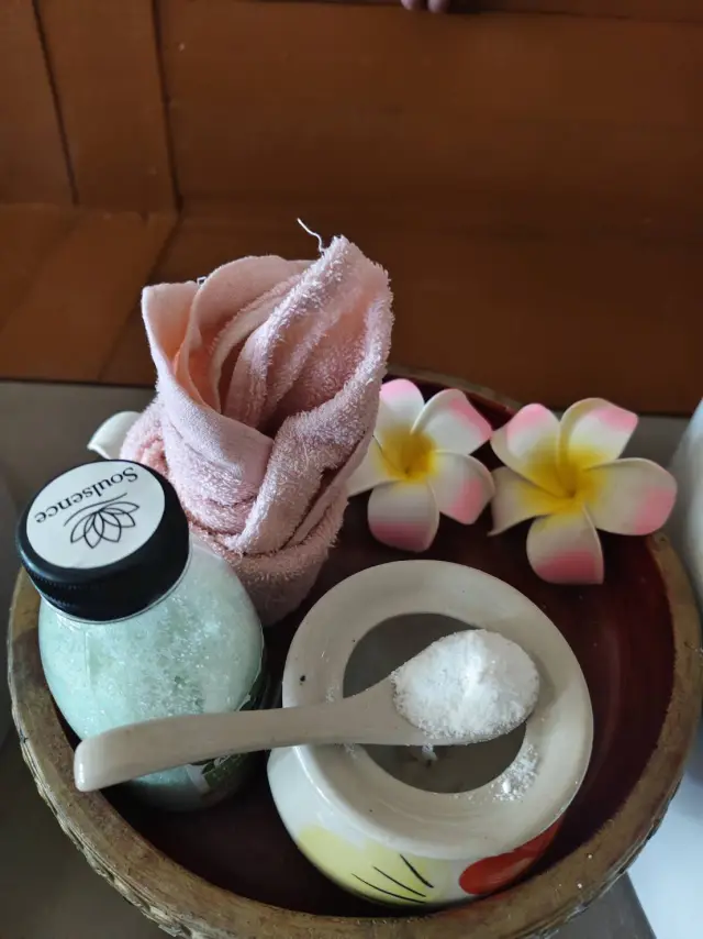 Pink towel, salt scrub bowl and spoon on a wooden tray used for spa treatments in Chiang Mai