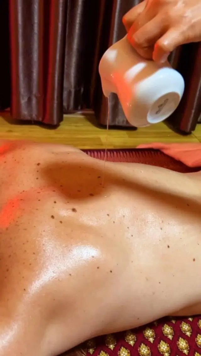 Warm oil being poured over a guest's back during an oil massage at Ai Oon Massage Lanna